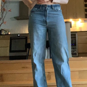Blå jeans med hög midja - Säljer ett par blå jeans med hög midja och loose straight passform. De har en klassisk design med fem fickor och en liten slitdetalj på bakfickan. Perfekta för en avslappnad stil.