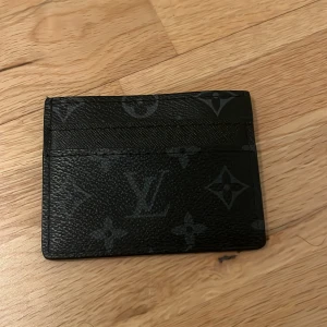 Svart plånbok - Säljer en stilren svart plånbok med det klassiska monogrammönstret. Plånboken har flera fack för kort och är tillverkad i ett slitstarkt material. Perfekt för att hålla dina kort organiserade med stil. 🖤