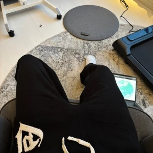 Svarta mjukisbyxor med tryck - Säljer ett par svarta mjukisbyxor med vitt tryck på ena benet. Byxorna har en bekväm passform med snörning i midjan. Perfekta för en avslappnad stil.