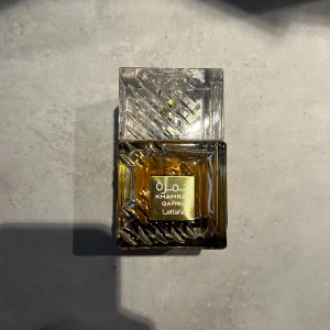 Khamrah Eau de Parfum från Lattafa - Säljer en elegant Khamrah Eau de Parfum från Lattafa. Flaskan har en unik design med ett mönstrat glas och en gyllene etikett. Parfymen har en djup bärnstensfärg som ger en lyxig känsla. Perfekt för den som vill ha en distinkt och minnesvärd doft. Som du ser på bild nummer 2 är den KNAPPT använd! Kan gå ner i pris