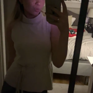 Beige ärmlös polotopp med knytband - Säljer en stilren beige ärmlös polotopp med knytband i midjan. Inga defekter och knappt använd