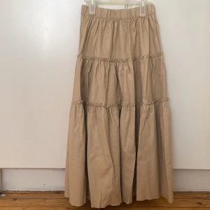 Beige skin långkjol från Gina Tricot - Säljer en beige långkjol från Gina Tricot. Kjolen har en volangdesign med flera lager och en elastisk midja för bekväm passform. Perfekt för en stilren och elegant look. Eftersom den inte har använt och är alltså helt ny så har den varit vikt ett tag. Men det försvinner när man hänger kjolen. 