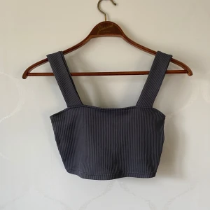 Grå ribbad linnetopp från H&M - Säljer en stilren grå ribbad linnetopp från H&M Divided. Toppen har breda axelband och en enkel design som passar perfekt till olika outfits. Perfekt för en avslappnad look eller att styla upp med accessoarer.