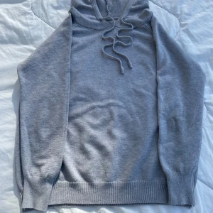 Stickad Grå hoodie med dragsko - Säljer en stilren grå hoodie med dragsko i halsen. Tröjan har långa ärmar och ribbade muddar vid ärmslut och nederkant. Perfekt för en avslappnad look. Tröjan är i riktgt bra skick och inga defekter jag vet om. Skriv till mig om  fler bilder eller frågor💛