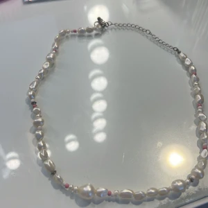 Halsband med vita pärlor och rosa detaljer - Elegant halsband med vita pärlor och små rosa detaljer. Justerbar kedja med karbinhake för enkel användning. Perfekt för att ge en stilren touch till din outfit.