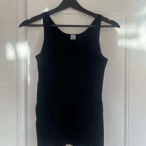 Svart ärmlös topp från Toteme - Säljer en stilren svart ärmlös topp från Toteme. Perfekt för lager-på-lager eller att bära som den är. Toppen har en klassisk rund halsringning och är tillverkad i ett mjukt material.