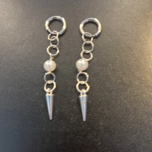 Silverörhängen med pärlor och spetsdetalj - Snygga silverörhängen med en kedjedesign som inkluderar vita pärlor och en spetsig detalj längst ner. Perfekta för att ge en edgy touch till din stil.