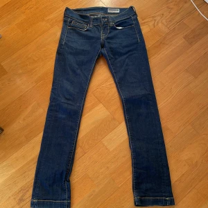 Mörkblå jeans från Fornarina - Snygga mörkblå lågmidjade jeans från Fornarina med dekorativa nitar på bakfickorna. Perfekta för en stilren look. Säljer då de är för små för mig, storleken är 26. Har små detaljer på bakfickan och nere vid fötterna som syns på näst sista bilden. Liten missfärgning längst ner på båda jeansen, syns i sista bilden.