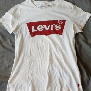 Vit t-shirt från Levi's - Säljer en klassisk vit t-shirt från Levi's med det ikoniska röda logotyptrycket på framsidan. T-shirten har en normal passform och är tillverkad i mjuk bomull. Perfekt för en avslappnad stil. 🕶️