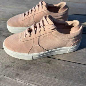 Rosa sneakers från Axel Arigato - Snygga rosa sneakers från Axel Arigato i mocka med vit sula. Skorna har en stilren design med snörning och diskret logga på sidan. Perfekta för en trendig look.