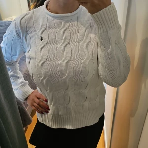 Vit stickad tröja från Ralph Lauren - Stilren vit stickad tröja från Polo  Ralph Lauren med klassiskt flätmönster. Tröjan har långa ärmar och en rund halsringning. Perfekt för en elegant och avslappnad look. 🧶✨