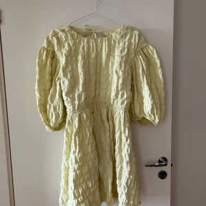 Weekday - Ljusgul klänning med puffärmar - Charmig ljusgul klänning från Weekday med puffiga trekvartsärmar och en öppen rygg. Klänningen har en texturerad yta och knytning i nacken. Perfekt för en somrig look!