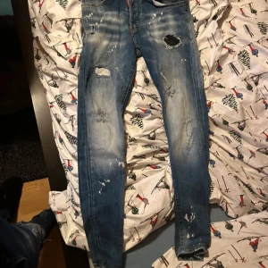 Blå jeans från Dsquared2 - Snygga blå jeans från Dsquared2 med slitna detaljer och en slim passform. Tillverkade i Italien, dessa jeans har en klassisk femficksdesign och en diskret logga på en röd etikett vid gylfen. Perfekta för en trendig look.
