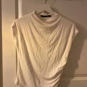 Vit topp från 157 - Säljer en stilren vit topp från 157 i storlek S. Toppen har en enkel design med korta ärmar och en rund hals. Perfekt för en avslappnad look. Materialet är mjukt och bekvämt. Med en reglad sida.