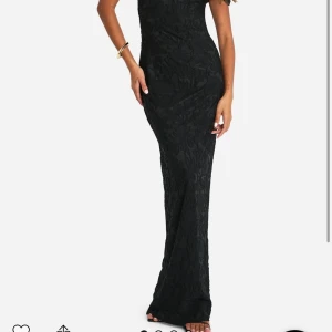 Svart långklänning med blommigt mönster - Elegant svart långklänning med ett subtilt blommigt mönster. Klänningen har en oneshoulder-design som ger en stilren look. Perfekt för speciella tillfällen. Ganska liten i storleken och tight i armarna. Har använts en gång🩵
