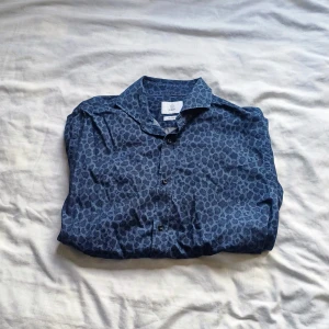 Denim leopardmönstrad skjorta - Snygg blå skjorta från Bläck med ett diskret mönster. Skjortan har långa ärmar och knappar framtill. Perfekt för en stilren look.