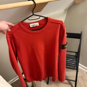 Röd tröja från Stone Island - Säljer en snygg röd tröja från Stone Island. Tröjan har långa ärmar och en rund halsringning. Den ikoniska Stone Island-loggan sitter på ärmen. Perfekt för en stilren look.