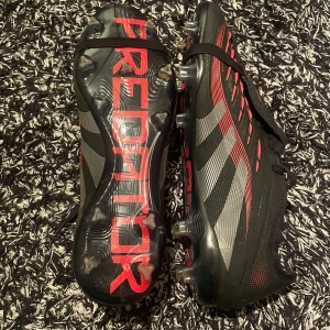 Adidas Predator  fotbollsskor  - Använda två träningar men passar inte riktigt min fot därav säljer jag dessa fotbollsskor. Storlek 46 2/3 men är väldigt små i storleken och är 29cm. Snygga Adidas Predator fotbollsskor i svart och röd med grå detaljer. Skorna har en modern design med snörning och en slitstark sula för optimalt grepp på planen. Perfekta för fotbollsspelare som vill ha både stil och funktion.
