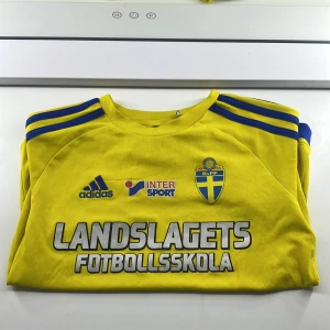 Gul Sveriges fotbollströja från Adidas - Säljer en gul fotbollströja från Adidas med blå detaljer och tryck från Landslagets Fotbollsskola. Tröjan har korta ärmar och är tillverkad i ett lätt och andningsbart material. Perfekt för fotbollsträning eller som supportertröja. Adidas logga och andra tryck på framsidan ger en sportig look. Barn t-shirt 9-10 år från Stadium 3 år sen. Jag har använt den 4-8 gånger . Den har lite skador men den kommer att inte synas. Priset kan diskuteras