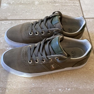 Gröna sneakers från Polo - Snygga gröna sneakers från Polo med vit sula och snörning. Skorna har en ovandel i textil och läder, samt en yttersula i gummi. Perfekta för en avslappnad stil. Box medföljer.