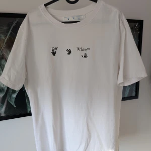 Vit t-shirt från Off-White - Säljer en vit t-shirt från Off-White med tryck på både fram- och baksida. Framsidan har en minimalistisk text och baksidan pryds av ett stort blått och vitt grafiskt mönster. Perfekt för dig som gillar streetwear och unika designer.