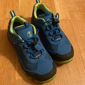 Kraftiga sneakers från Trollkids str 34 - Säljer ett par blå sneakers från Trollkids med svarta och gröna detaljer. Skorna har snörning och en robust sula som ger bra grepp. Perfekta för utomhusaktiviteter och äventyr.
