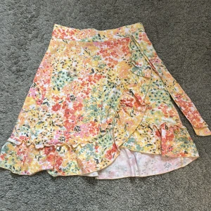 Blommig kjol från Gina Tricot - Säljer en färgglad blommig kjol från Gina Tricot i storlek XS. Kjolen har volangdetaljer och ett knytband i midjan. Perfekt för en somrig look! 🌸