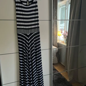 Randig långklänning från Yachting Time - Snygg randig långklänning från Yachting Time i svart och vit. Klänningen har ett coolt mönster med horisontella ränder och en liten röd broderad detalj. Perfekt för en avslappnad dag med stil.