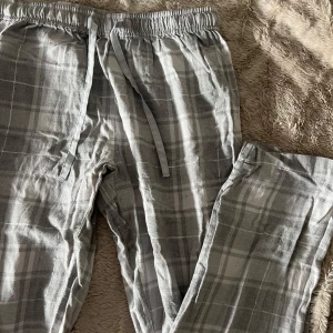 Grå och vit rutiga pyjamasbyxor - Säljer ett par bekväma grå och vit rutiga byxor med elastisk midja och snörning. Perfekta för en avslappnad stil.