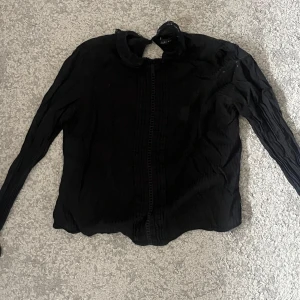 Svart blus med spetsdetaljer - Snygg svart blus med spetsdetaljer vid halsen. Perfekt för en elegant look. Blusen har långa ärmar och en fin passform. Från Zara i storlek XS