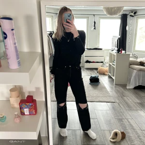 Svarta jeans med slitningar - Säljer ett par svarta jeans med coola slitningar vid knäna. De har en hög midja och en straight passform som ger en avslappnad look. Perfekta för en trendig stil!