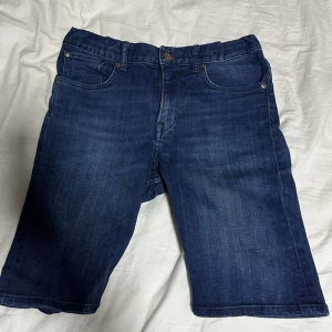 Mörkblå jeansshorts - Snygga mörkblå jeansshorts med klassisk femficksdesign och knappgylf. Perfekta för en avslappnad stil under varma dagar. De har en normal passform och är tillverkade i slitstarkt denim.