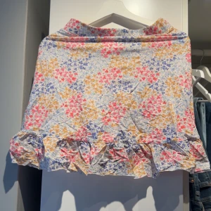 Blommig kjol med volang - Charmig blommig kjol i ljusa färger med volangdetaljer längst ner. Liten i storlek.