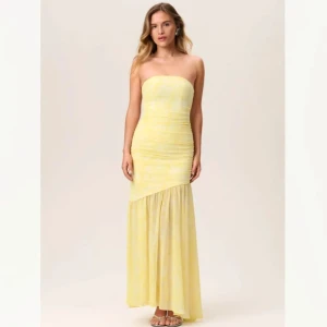 Axelbandslös blommig klänning - Säljer en Helt ny axelbandslös klänning från Adoore i en härlig mix av gul och vit . Klänningen har en lång design med en tajt passform upptill och en mer utsvängd kjol nedtill, perfekt för somriga tillfällen.  Det är den gula klänningen jag säljer, men hade bara bild på den oranga på men dem är samma modell och samma storlek! (Bilderna på den orangea är mina) 