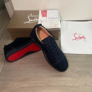 Svarta sneakers från Christian Louboutin - Snygga svarta sneakers från Christian Louboutin med den ikoniska röda sulan. Skorna har snörning och är tillverkade i mocka, vilket ger en lyxig känsla. Perfekta för den som vill ha stil och komfort i ett.