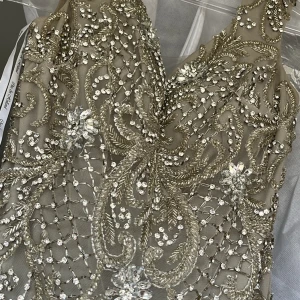 Beige klänning med pärlor och paljetter - Elegant beige klänning med v-ringad design, dekorerad med glittrande pärlor och paljetter. Perfekt för en glamorös kväll.