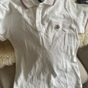 Vit polotopp från Moncler - Säljer en stilren vit polotopp från Moncler med klassisk krage och knappar framtill. Fick den i present men har aldrig använt för att den inte passa mig, den är äkta taggsen är kvar och har tyvärr inget kvitto. 
