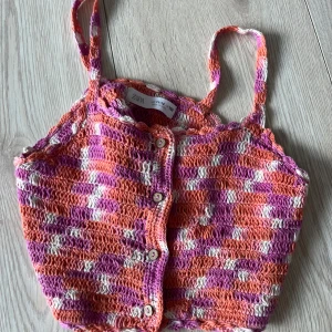 Färgglad virkad topp från Zara - Säljer en färgglad virkad topp från Zara i storlek 152. Toppen har smala axelband och knappar framtill. Den är mönstrad i rosa, orange och vit med en härlig sommarkänsla. Perfekt för varma dagar!🩷🩷