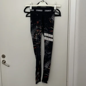 Mönstrade leggings från Stronger - Snygga leggings från Stronger med ett unikt mönster i svart, vitt och orange. De har en hög midja och är perfekta för träning. Materialet är stretchigt och bekvämt, vilket ger en bra passform.