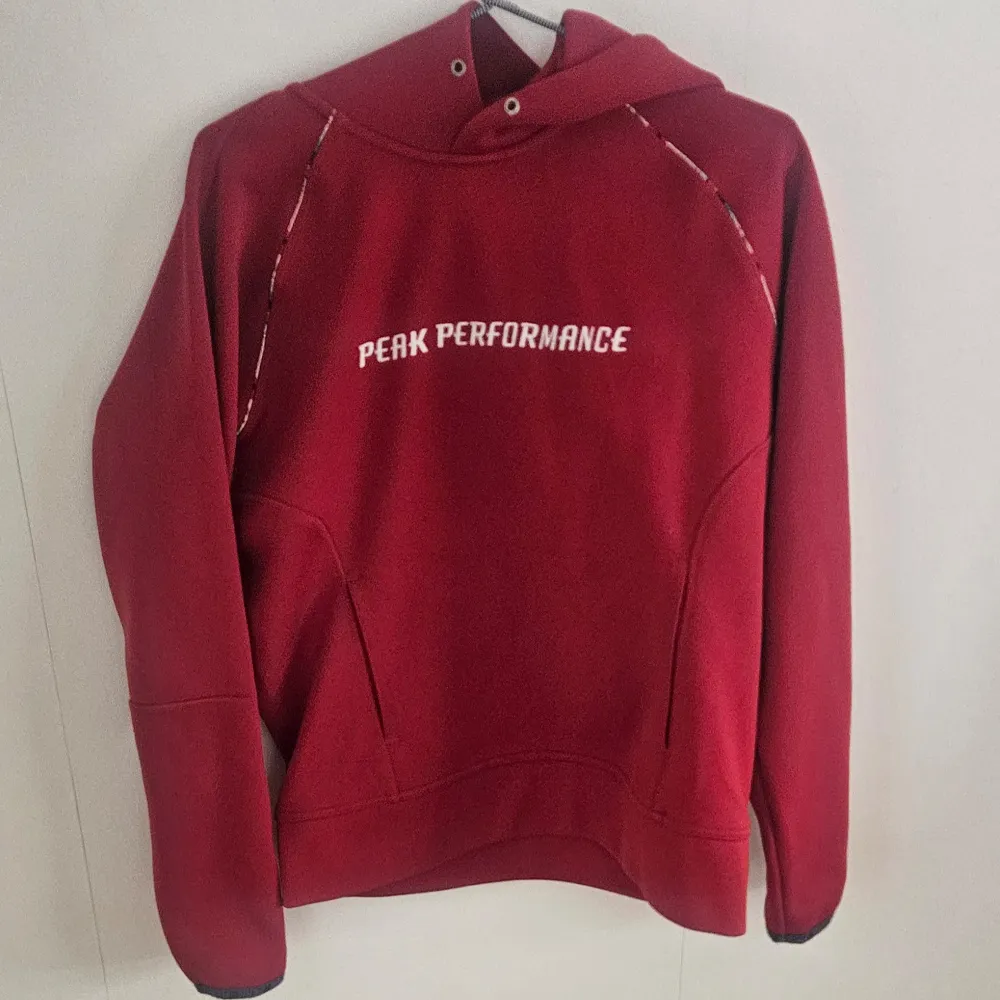 Säljer en snygg röd hoodie från Peak Performance RD med vit logga på bröstet. Hoodien har en justerbar huva och långa ärmar. Perfekt för kyliga dagar eller som ett stilrent vardagsplagg. Storlek M . Neuletakit & Villapaidat.