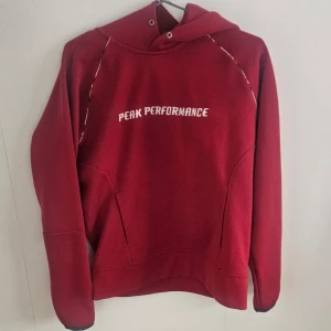 Röd RD hoodie från Peak Performance strl M - Säljer en snygg röd hoodie från Peak Performance RD med vit logga på bröstet. Hoodien har en justerbar huva och långa ärmar. Perfekt för kyliga dagar eller som ett stilrent vardagsplagg. Storlek M 