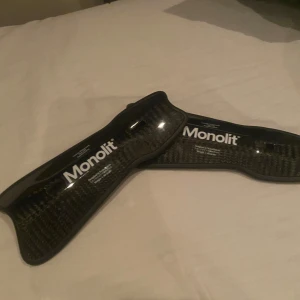 Svarta benskydd från Monolit - Säljer ett par svarta benskydd från Monolit, designade i Skandinavien. Tillverkade i kolfiber för lätt och starkt skydd. Perfekt för fotbollsspelare som söker högkvalitativ utrustning.