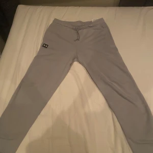 Grå mjukisbyxor från Under Armour - Säljer ett par grå mjukisbyxor från Under Armour. Byxorna har en loose passform och är tillverkade i ett mjukt material. Perfekta för en avslappnad stil. De har en elastisk midja med snörning för justerbar passform.