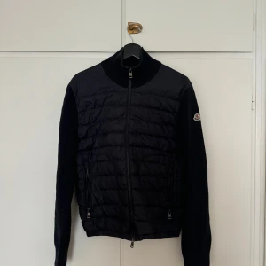Moncler Cardigan - Navy - Snygg blå cardigan från Moncler med quiltad framsida och dragkedja. Jackan har långa ärmar och en hög krage. Perfekt för kyligare dagar. Säljes pga att den är för liten. Jackan är i storlek M(2).