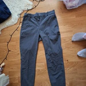Grå kostymbyxor från H&M - Snygga grå kostymbyxor från H&M med en stilren design. Byxorna har en dragkedja och knappar i midjan för en säker passform. Perfekta för en elegant look.