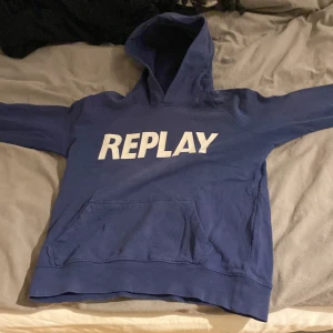 Blå hoodie från Replay - Säljer en snygg blå hoodie från Replay med stor vit logga på framsidan. Tröjan har en klassisk känguruficka och en bekväm huva. Perfekt för en avslappnad stil.