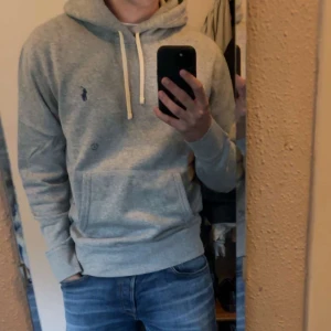 Grå hoodie från Polo Ralph Lauren för 1000kr - Säljer en stilren grå hoodie från Polo Ralph Lauren. Tröjan har en klassisk design med huva och dragsnören samt en liten logotyp på bröstet. Perfekt för en avslappnad look. Pris kan diskuteras 