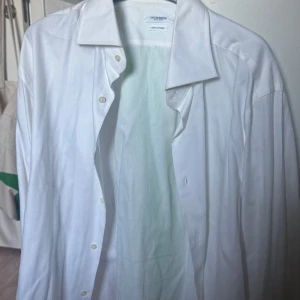 Vit skjorta från Gutteridge - Säljer en klassisk vit skjorta från Gutteridge, tillverkad i 100% bomull. Skjortan har en stilren design med knappar framtill och en traditionell krage. Perfekt för en elegant look.