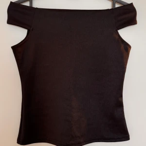 Svart ribbad off-shoulder topp - Snygg svart ribbad off-shoulder topp. Perfekt för en utekväll eller ett annat festligt tillfälle. Toppen är i väldigt bra skick och har en tidlös stil som passar till många outfits! Dock är lappen tyvärr avklippt så vet inte märket.