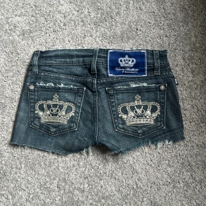 Victoria beckham Jeansshorts - Snygga jeansshorts från vicktoria bechand med fransiga kanter och broderade kronor på bakfickorna. Perfekta för en avslappnad sommarlook. De har en klassisk femficksdesign och låg midja.